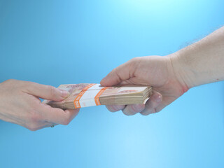 Obraz premium Woman's hand gives stack of cash to man's hand on blue background