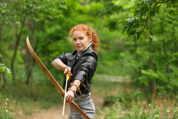 Sporty young woman practicing archery outdoors