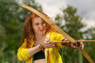 Sporty young woman practicing archery outdoors