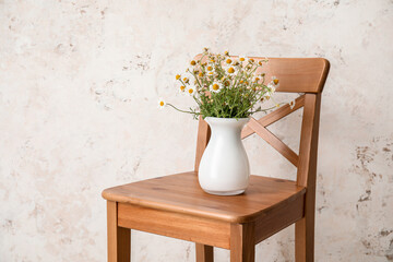 Vase with beautiful chamomiles on chair against light background