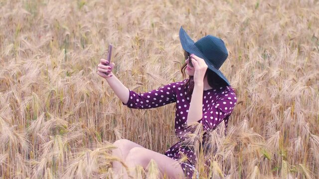 Attractive fun hippie woman in the wheat field at sunset making a selfie with smartphone