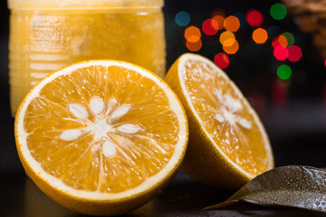 Close-up of halved orange next to a glass of orange juice with orange leaves and background with bokeh