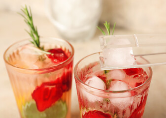 Putting of ice cube into glass with fresh strawberry lemonade on table