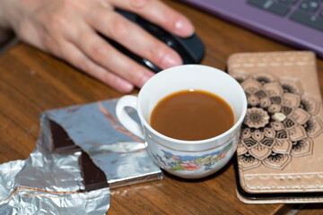 Self-isolation. Working remotely. A woman's hand with a mouse, laptop, coffee mug, phone and chocolate.