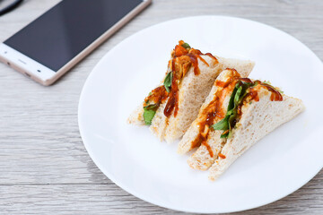 Close view of grilled chicken sandwich in white plate on wooden table 