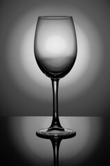 transparent wine glass on black glass with round illumination at the back