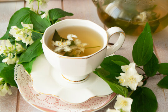 a mug of herbal tea and jasmine flowers on a white wooden table, vintage cup and jasmine flowers