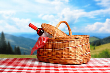 Picnic basket with bottle of wine on checkered tablecloth in park