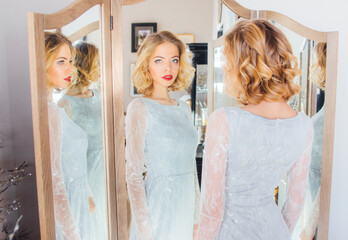 Beautiful blond girl with vintage make up and hairstyle staying near triple mirror - 358429564