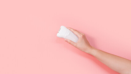 Female holding white depilator against pink colored background. Removal hair. Minimalism. Top view. Body hygiene, spa procedures banner