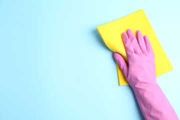 Person in rubber glove with rag on light blue background, closeup of hand. Space for text