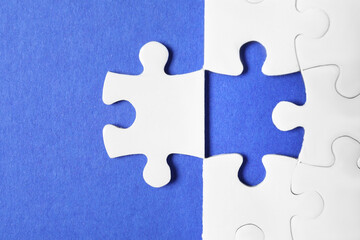 Blank white puzzle with separated piece on blue background, flat lay