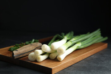 Fresh green spring onions and knife on wooden board, closeup