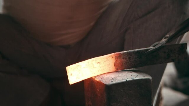 Hot metal piece being hammered by a heavy hammer on a square anvil