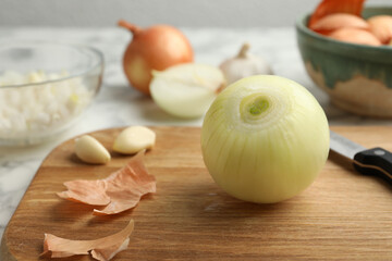 Peeled onion and knife on wooden board, closeup