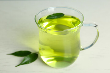 Cup of aromatic green tea and leaves on light wooden table