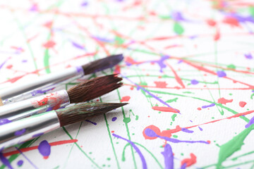 Brushes on canvas with colorful paint splashes, closeup. Art and creativity