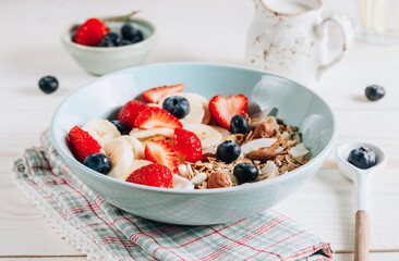 Healthy breakfast bowl with oat granola with dried buckwheat, nuts and coconut chips, berries and rice milk
