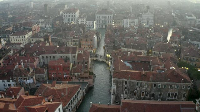 Aerial, tilt. drone shot towards people walking on a bridge, over a small channel, at the Strada nova street, evening, in Venice city, Italy
