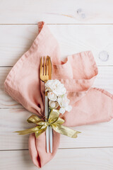 Festive table setting. Cutlery with pink napkin and gift box on white wooden background.