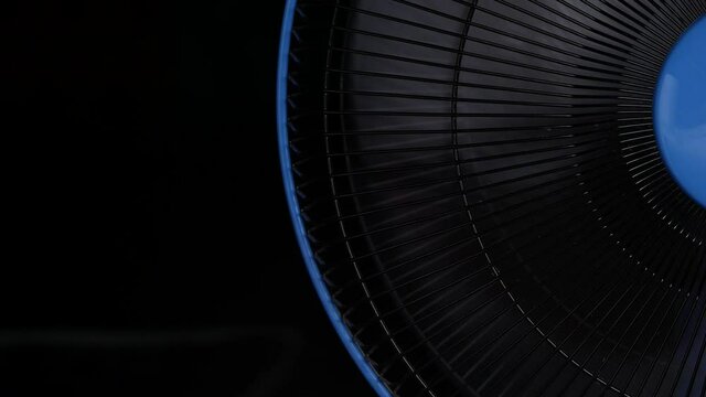 Close-up turning of the electric fan blades with grill isolated on dark background.