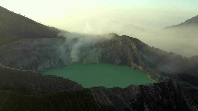 Aerial shot of idyllic lake and rocky mountains against sky, drone flying forward over natural landscape at sunset - East Java, Indonesia