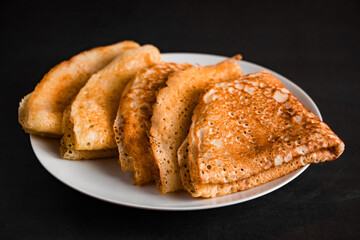 Thin pancakes on a plate on a black background, traditional Russian food.