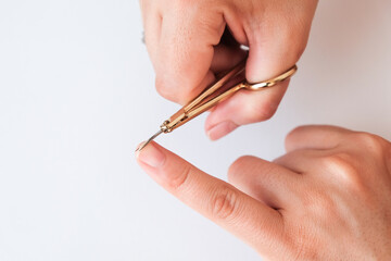 Woman hands using a small scissors to cut her fingernails on a white background. View from above. Manicure at home
