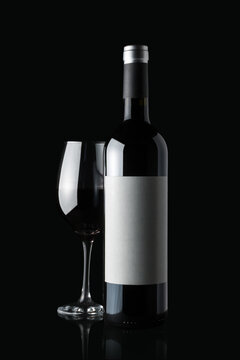 Glass of red wine next to a bottle isolated on black background