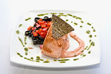 salmón con pasta, trozo de salmón asado sobre pasta negra adornado con piel de pescado crocante y pimiento morrón rojo, sobre fondo blanco