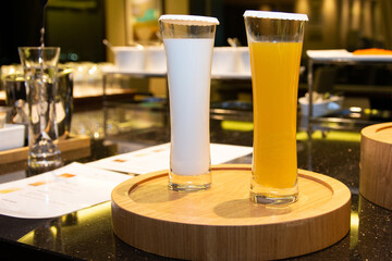 Long drinking glasses with white and orange cokctail drink inside. Tall cocktail glasses on a wooden stand.
