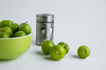 Big size,green color,fresh plums in a stylish bowl on the white background with salt and metal salt shaker