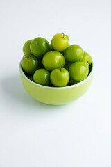 Ripe,fresh green plums in the green color bowl on the white surface with copy space.Vertical image.