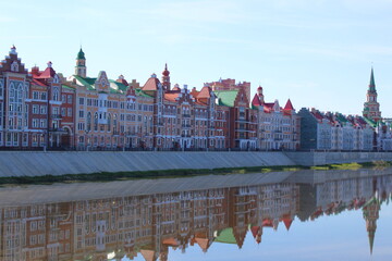 Fototapeta premium Town house stands on the river bank and is reflected in the water on a summer morning