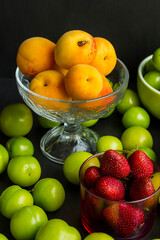 Apricot in the stylish,transparent glass bowl on the black surface with plums and strawberries.Vertical image.