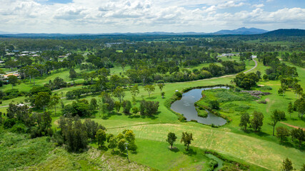 Fototapeta na wymiar Vibrant green summer landscape showing a golf course and hills in the distance, in Calliope, Queensland