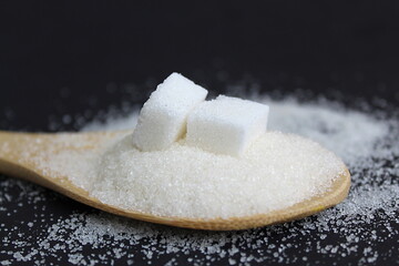 Fototapeta na wymiar Friable sugar on a wooden spoon on a black background