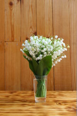 A bouquet of lilies of the valley stands in a vase on a wooden table