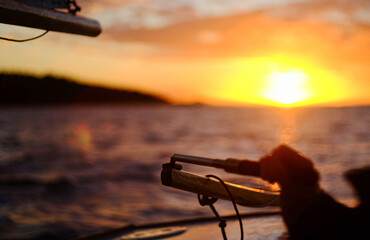 Detail of rodder and skipper's hand on small sailing boat in vast seascape at sunset between Bird...