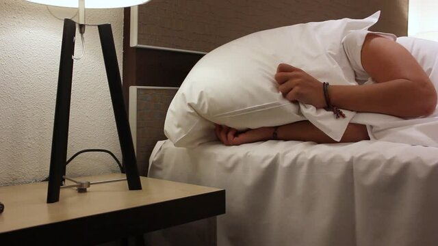 Young girl in bed struggling with insomnia covering her face with pillow