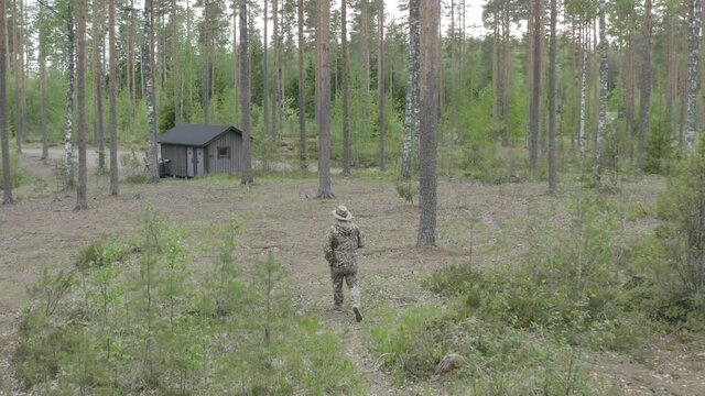Drone view of man in camouflage walking in the woods near a forest house.