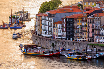 Fototapeta na wymiar Facades of traditional colorful houses in Ribeira and rabelo boats on Douro at sunset golden hour in Porto, Portugal
