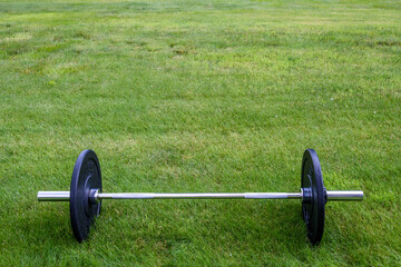 Olympic barbell with black weight plates on a green lawn, ready for an outdoor workout
