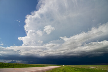 The sun shines brightly on a highway with a dark thunderstorm over the horizon.