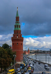 Fototapeta premium Red Kremlin wall and tower, traffic on Kremlevskaya Embankment by the Moskva River with a cloudy sky in Moscow, Russia