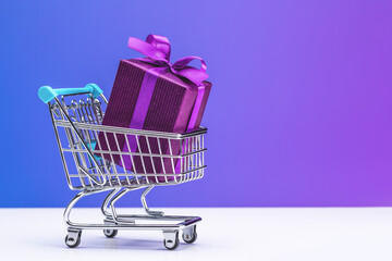 Surprise in purple box tied with satin ribbon. Gift in shopping cart (toy).