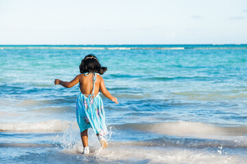 Little girl in beautiful blue dress enjoying white sandy caribbean tropical beach jumping running and having fun in the ocean sea waves 
