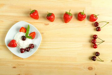 Ice cream dessert with strawberries and cherries in a plate on a wooden table and next to the berries. Copy space.