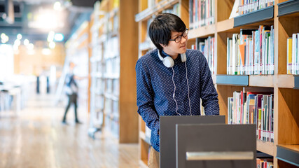 Young Asian man university student pushing book cart in college library finding textbook for...