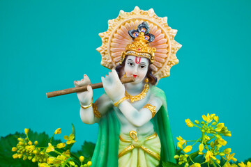 Hindu god Krishna. Statue with flowers on a blue background.